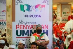 Seorang pria duduk di depan spanduk UMNO (United Malays National Organisation) dan PAS (Pan-Malaysian Islamic Party) saat acara resmi bergabung dengan aliansi di Kuala Lumpur, Malaysia, Sabtu, 14 September 2019. (Foto: AP)