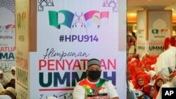 FILE - A man sits in front of banners of UMNO (United Malays National Organization) and PAS (Pan-Malaysian Islamic Party) during an event to announce an alliance between the two in Kuala Lumpur, Malaysia, Sept. 14, 2019.