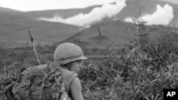 A U.S. Marine pinned down by sniper fire, looks back to check on his buddies as white phosphorous artillery rounds mark major Viet Cong position, action took place 15 miles south, southwest of Da Nang, Jan. 29, 1967. 