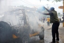 Local journalist throws water on burning vehicle that belongs to Radio Tele-Guinen in Port-au-Prince, Haiti, June 10, 2019.
