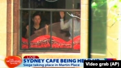 This image taken from video shows people holding up hands inside a cafe in Sydney, Australia, Dec. 15, 2014. 