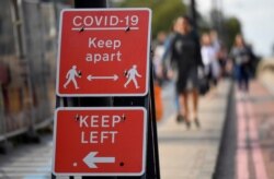 FILE - Pedestrians walk near public health signs in London, September 11, 2020.