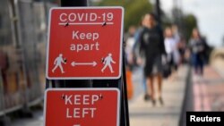 FILE - Pedestrians walk near public health signs in London, Britain, Sept. 11, 2020. 