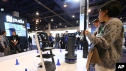 FILE - People check out the Pudu delivery robots at the Pudu booth during the CES tech show, Jan. 8, 2020, in Las Vegas. 