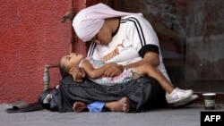 A Syrian refugee woman holds her child as they rest on the sidewalk of a street in the southern Lebanese city of Sidon.