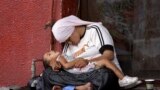 A Syrian refugee woman holds her child as they doze off on the sidewalk of a street in the southern Lebanese city of Sidon. The exodus of Syrian refugees accelerated dramatically in recent months, with over 1 million refugees arriving in the first five months of 2013 alone.