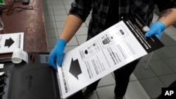 A poll worker at the Su Nueva Lavanderia polling place uses rubber gloves as she enters a ballot in the ballot box in Chicago, March 17, 2020.