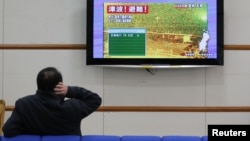 A man scratches his head as he watches television showing live camera footage from Ishinomaki, Miyagi prefecture and an alert sign that reads,"Tsunami! Evacuate!" at Nagano train station, central Japan December 7, 2012