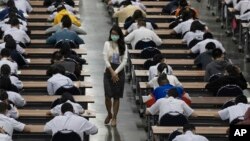 A teacher wears a protective mask as middle school students take an entrance examination for high school in Bangkok, Thailand, Thursday, March 5, 2020.