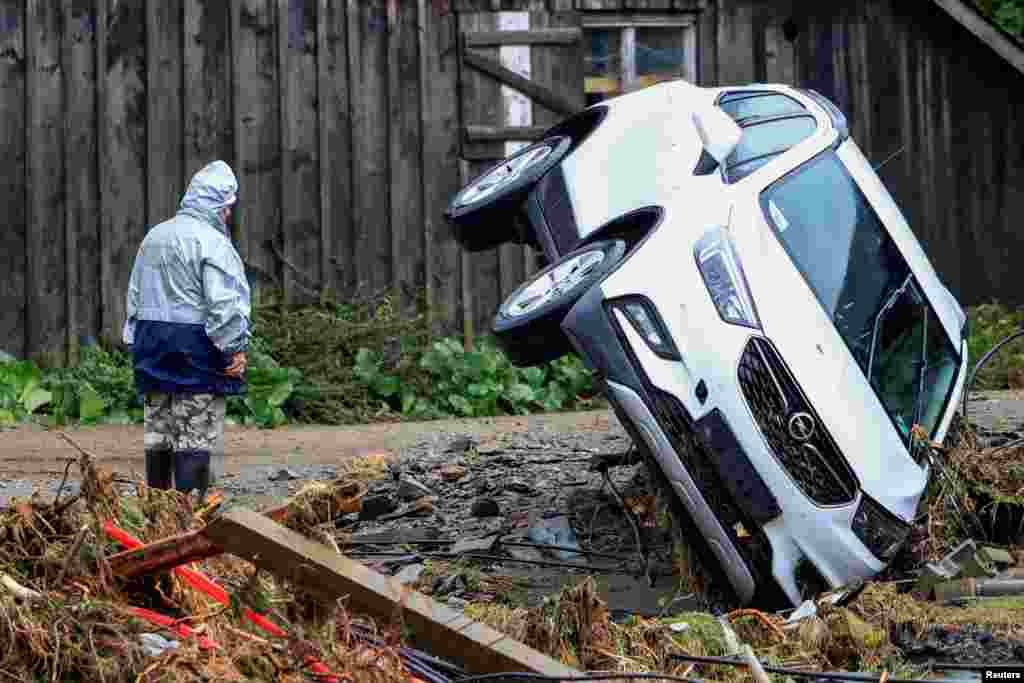 A person stands next to an overturned vehicle, following heavy rainfalls in Bela pod Pradedem, near Jesenik, Czech Republic.