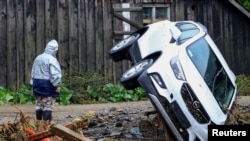 A person stands next to an overturned vehicle, following heavy rainfalls in Bela pod Pradedem, near Jesenik, Czech Republic.