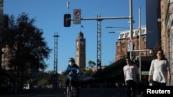 A bicycle delivery courier and pedestrians make their way through an intersection in the city center following the easing of restrictions implemented to curb the spread of the coronavirus disease (COVID-19) in Sydney, Australia, June 16, 2020. 