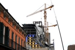 Workers in a bucket hoisted by a crane begin the process of preparing the two unstable cranes for implosion at the collapse site of the Hard Rock Hotel, which partially collapsed while under construction, Oct. 12, 2019, in New Orleans.