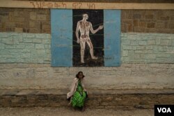 A woman sits in front during a science lesson painted on a wall of one school now housing displaced families, in Mekelle, Ethiopia, June 3, 2021. (Yan Boechat/VOA)