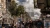 People walk along a street as a plume of smoke rises in the background during an Israeli strike on the Bureij refugee camp in the central Gaza Strip on November 2, 2023, as battles between Israel and the Palestinian Hamas movement continue. (Photo by MAHM