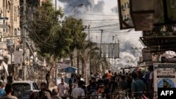 People walk along a street as a plume of smoke rises in the background during an Israeli strike on the Bureij refugee camp in the central Gaza Strip on November 2, 2023, as battles between Israel and the Palestinian Hamas movement continue. (Photo by MAHM