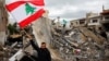 (FILE) A man waves a Lebanese flag as he stands amidst the rubble of a building destroyed in Israeli strikes, after a ceasefire between Israel and Hezbollah took effect in Tyre, Lebanon, November 27, 2024.