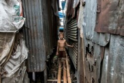 FILE - A boy walks on a bamboo bridge by his home in a poor community on the outskirts of Yangon, May 21, 2021.