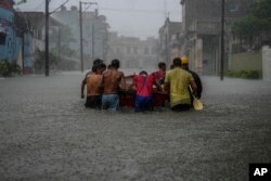 FILE - Residents push a boat through a flooded street to rescue a neighbor unable to leave his home on his own during a tropical cyclone in Havana, Cuba on June 3, 2022. (AP Photo/Ramon Espinosa, File)