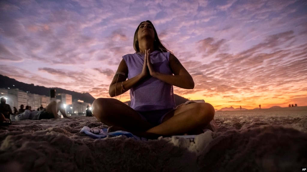 FILE - A woman sits in lotus prayer pose during the "Yoga at the Sunrise" event on Copacabana beach, in Rio de Janeiro, on June 22, 2024. (AP Photo/Bruna Prado)