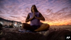 FILE - A woman sits in lotus prayer pose during the "Yoga at the Sunrise" event on Copacabana beach, in Rio de Janeiro, on June 22, 2024. (AP Photo/Bruna Prado)