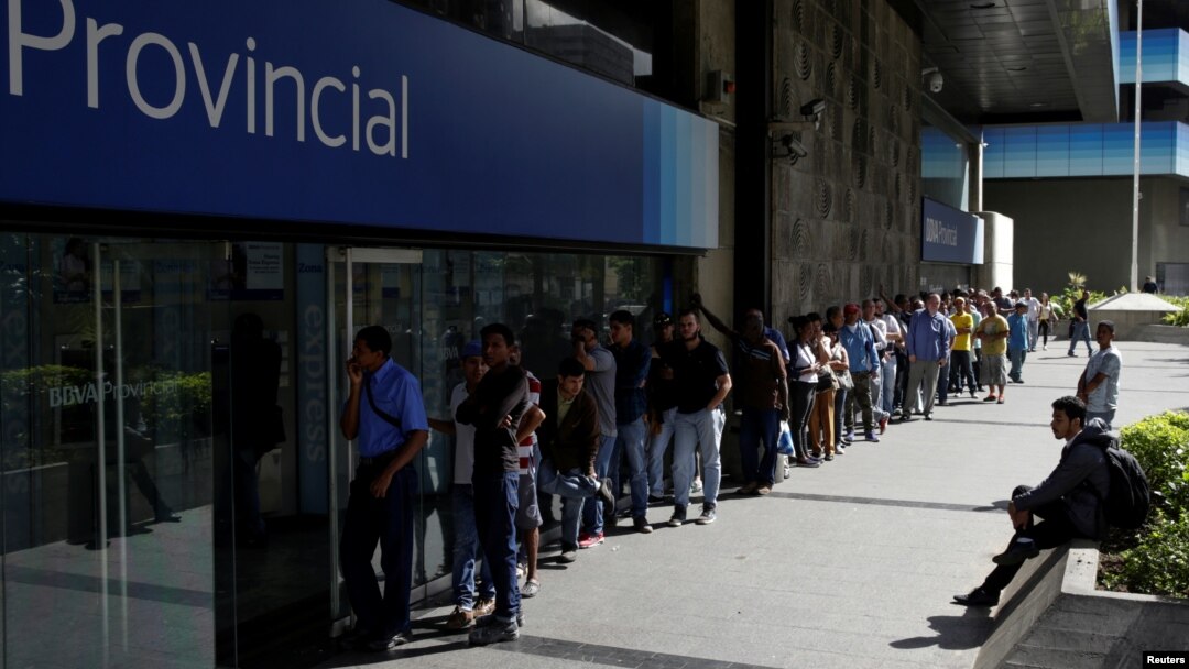 People line up to withdraw cash from an automated teller machine outside a Banco Provincial branch in Caracas, Venezuela, Dec. 12, 2016.