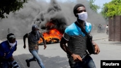 ARCHIVO - Hombres corren junto a neumáticos en llamas durante una protesta que exige el fin de la violencia de las pandillas, en Puerto Príncipe, Haití, el 14 de agosto de 2023.