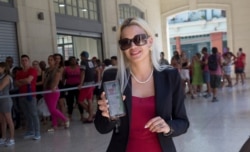 Claudia Santander, a 21-year-old graphic designer, poses with her mobile phone as others line up to buy goods at the 4 Caminos market in Havana, Cuba, March 11, 2020. Santander administers 10 Whatsapp groups that help others search for necessities.