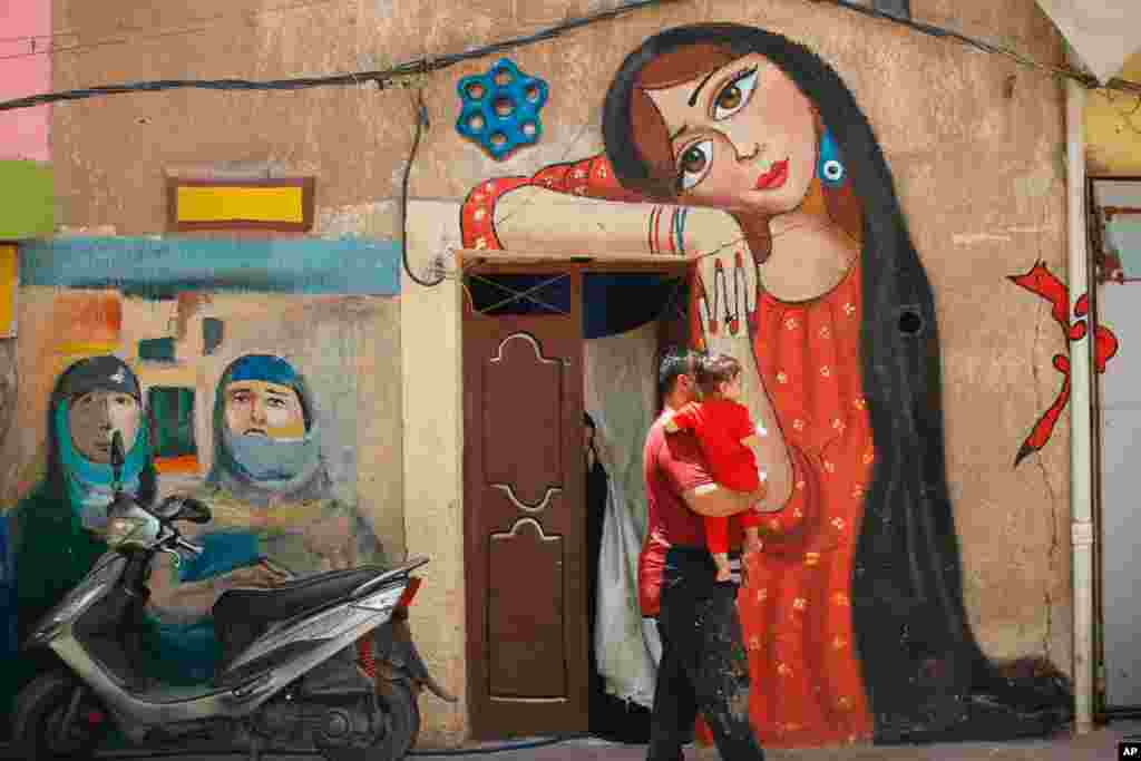 Artist Ali Khalifa, center, holds his daughter in front of a mural he painted, in the Kadhimiya district of Baghdad, Iraq.