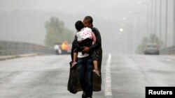 یک پناهجوی اهل سوریه در حال بوسیدن فرزند خود و راه رفتن در زیر باران به سمت مرز مشترک مقدونیه با یونان