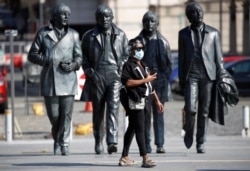 A woman wears a face mask as she stands in front of a statue of The Beatles following the outbreak of the coronavirus disease in Liverpool, Britain, Sept. 21, 2020.