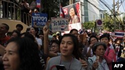 Thai supporters stand beside an electoral campaign poster of prime minister Yingluck Shinawatra (top) as they cheer on anti-government protesters marching along the streets in downtown Bangkok, Jan. 30, 2014. 