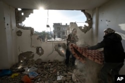 FILE - Palestinians collect their belongings from their damaged house after an Israeli airstrike in Rafah, southern Gaza Strip, January 27, 2024.