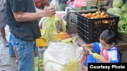 Seorang pedagang di pasar Cisarua, Bogor, mengupas kulit jagung dibantu anaknya yang masih kecil.