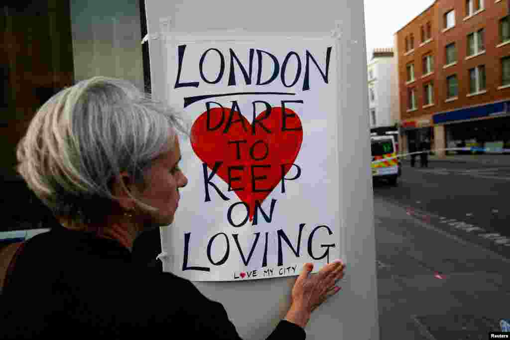 A woman attaches a sign near London Bridge, where attackers rammed a hired van into pedestrians and stabbed others nearby, June 4, 2017.