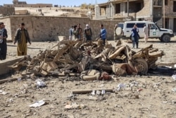 Security personnel and residents gather around the site of a car bomb attack that targeted an Afghan police headquarters in Feroz Koh, the capital of Ghor Province, Oct. 18, 2020.