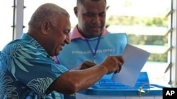 Pemimpin militer Fiji, Voreqe Bainimarama (kiri) memasukkan surat suaranya ke dalam kotak penitipan suara di Suva, Fiji (17/9).