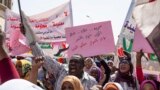 FILE - Protesters carry posters in Arabic that say, "Freedom, justice, and peace, and the revolution is the choice of the people," at the sit-in outside the military headquarters, in Khartoum, Sudan, May 2, 2019.