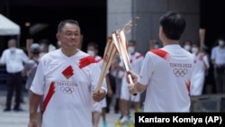 Le président du Comité olympique japonais, Yasuhiro Yamashita, à gauche, effectue un baiser de la torche lors de l'événement final du relais de la torche pour les Jeux olympiques de Tokyo au complexe du gouvernement métropolitain de Tokyo, vendredi 23 juillet 2021.