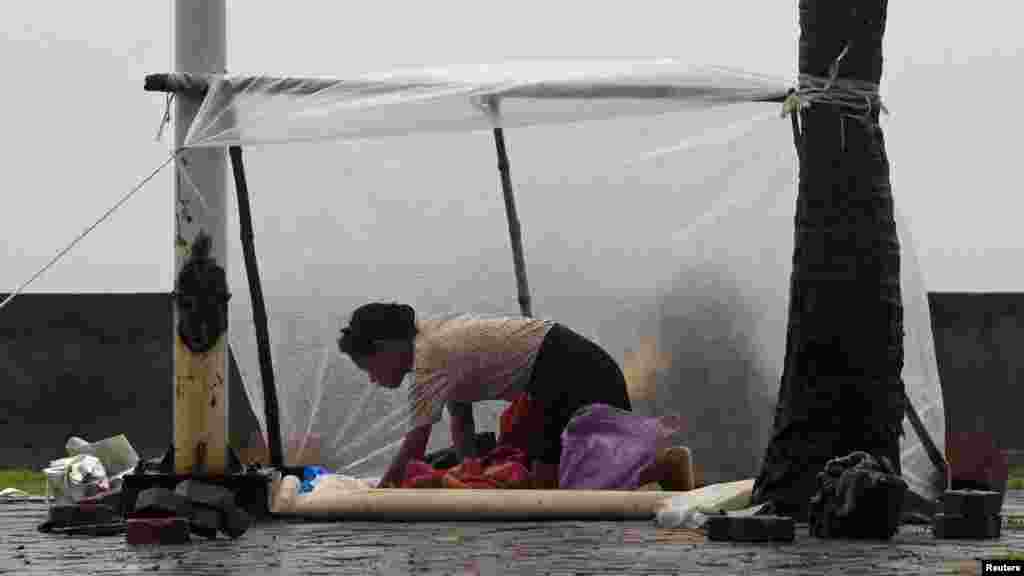 A woman shields herself with a plastic sheet from the rain brought on by Typhoon Kalmaegi, also called Luis, on the street at a bay in Manila, Philippines, Sept. 14, 2014. 