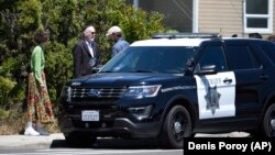 Tiga orang menunggu di luar sinagoga Poway, California sementara polisi mengamankan sinagoga pasca penembakan dan menahan seorang tersangka, Sabtu (27/4). 