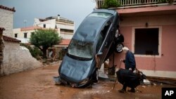 A man walks past a car moved by the force of flood water and a damaged house in the town of Mandra western Athens, Nov. 16, 2017. Greece's fire department says rescue crews are searching for six people reported missing in the western Athens area following major flash flooding that left at least 16 people dead.