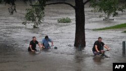 Orang-orang mengendarai sepeda melalui sebuah taman yang tergenang banjir di tepi sungai Nepean di pinggiran Penrith, saat kota Sydney, Australia, bersiap menghadapi banjir terburuk dalam beberapa dekade, Minggu 21/3. (Foto: AFP)