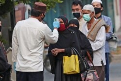 FILE - Officials take the body temperature reading of worshippers as a precaution against the new coronavirus outbreak, outside a mosque in Jakarta, Indonesia, July 31, 2020.
