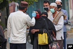 FILE - Officials take the body temperature reading of worshippers as a precaution against the new coronavirus outbreak, outside a mosque in Jakarta, Indonesia, July 31, 2020.