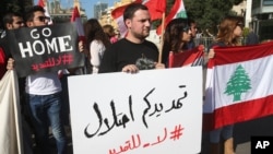 FILE - Activists hold Lebanese flags and an Arabic placard, center, that reads:"Your extension is an occupation, no to the extension," during a protest against the extension of the Lebanese parliament, on a road that leads to the Parliament building, in downtown Beirut, Lebanon.