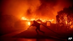 Um bombeiro combate o incêndio de Palisades enquanto este queima uma estrutura no bairro de Pacific Palisades, em Los Angeles, na terça-feira, 7 de janeiro de 2025.