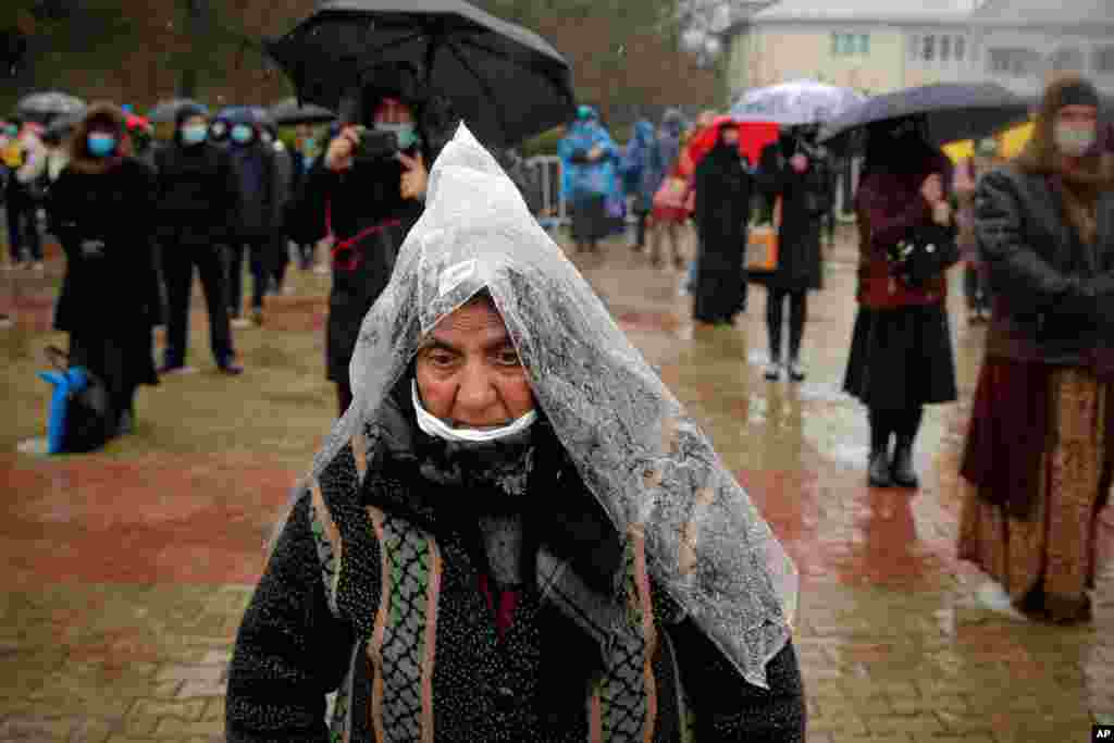A woman using a plastic sheet as rain protection attends a religious service celebrating St. Andrew in the village of Ion Corvin, eastern Romania. 