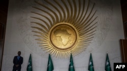 FILE - A security guard stands next to an AU logo at the entrance of the main plenary hall during the second day of the 37th Ordinary Session of the Assembly of the African Union at the AU headquarters in Addis Ababa on February 18, 2024. 