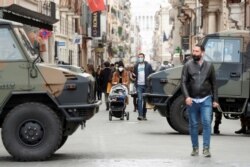 People walk past army vehicles at a street on the final day of open restaurants and bars before tighter coronavirus disease (COVID-19) restrictions are enforced, in Rome, Italy, March 14, 2021.